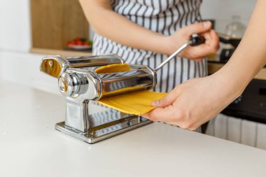 Önlüklü adam makarna kesicili spagetti yapıyor. Evde yakın çekim makarna pişirme. Parlak sarı hamurdan yemek hazırlıyorum..