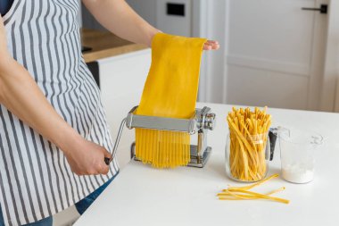 Önlüklü adam makarna kesicili spagetti yapıyor. Evde yakın çekim makarna pişirme. Parlak sarı hamurdan yemek hazırlıyorum..