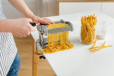 Önlüklü adam makarna kesicili spagetti yapıyor. Evde yakın çekim makarna pişirme. Parlak sarı hamurdan yemek hazırlıyorum..