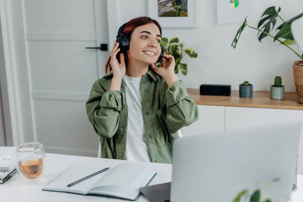 Woman listening music with wireless headphones. Young businesswoman relaxing at comfortable workplace. Concept of resting during online business at home office,telework or studing. Happy girl singing.