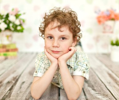 kıvırcık kahverengi gözlü çocuk bej gömlek ve pantolon yalanlar üzerine bir ahşap zemin parlak bir odada - portre