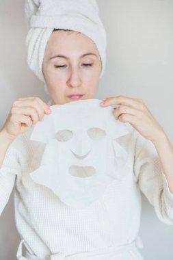 Bornozlu ve kafasında havlu olan kolajen maskeli bir kadın.