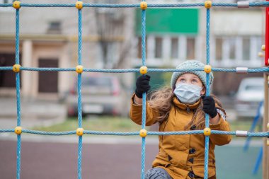 Tıbbi maskeli küçük bir kız. Sonbahar çocuk parkında