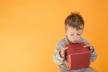 Süveterli çocuk turuncu arka plandaki hediyeye bakıyor.