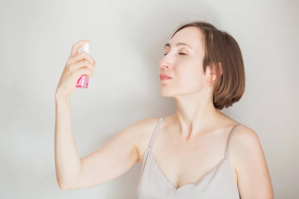 European brunette woman applying face tonic on light grey background — Stock Photo, Image