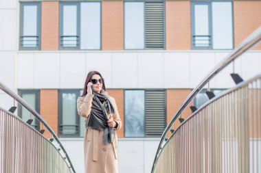 Palto giymiş Avrupalı bir kadın telefonda konuşuyor. Sonbahar şehrinde