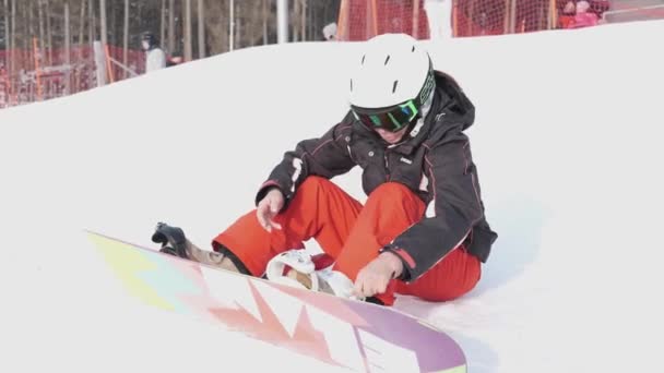 Старшая кавказка в спортивной одежде, сидит на сноуборде и готовится к поездке — стоковое видео
