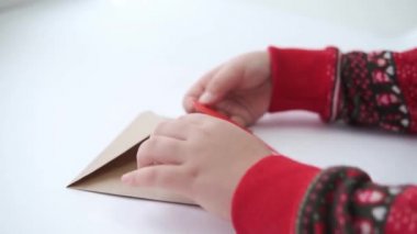 Çocuk elleri kırmızı kağıt kalbi el işi zarfına koyar. Çevre dostu sevgililer günü