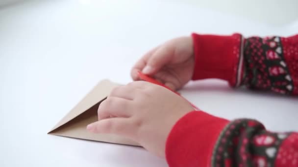 Manos de los niños ponen el corazón de papel rojo en el sobre artesanal. Día de San Valentín ecológico — Vídeo de stock