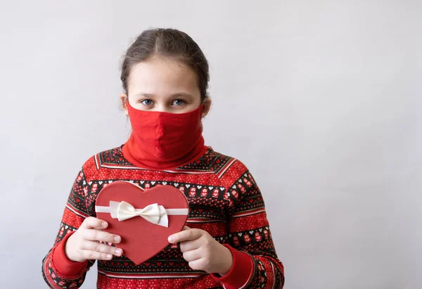 Jolie petite fille en robe rouge avec coeur boîte cadeau masque visage Saint Valentin. — Photo