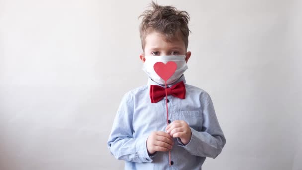 Schattig jongetje in strikje met hartje op stok en gezichtsmasker Valentijnsdag. — Stockvideo