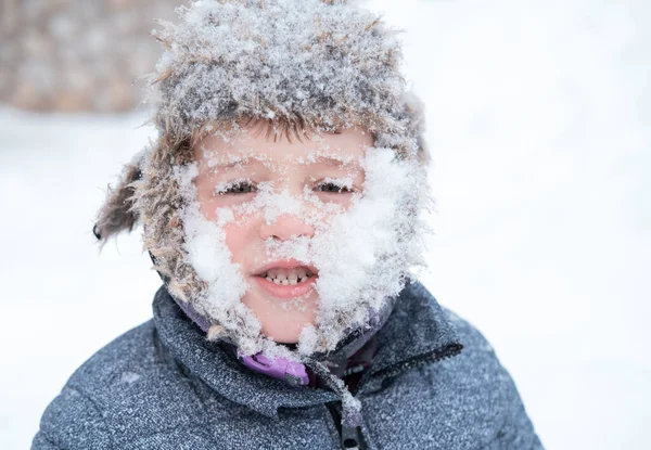 Kleine schattige jongen in winterhoed met besneeuwd gezicht — Stockfoto