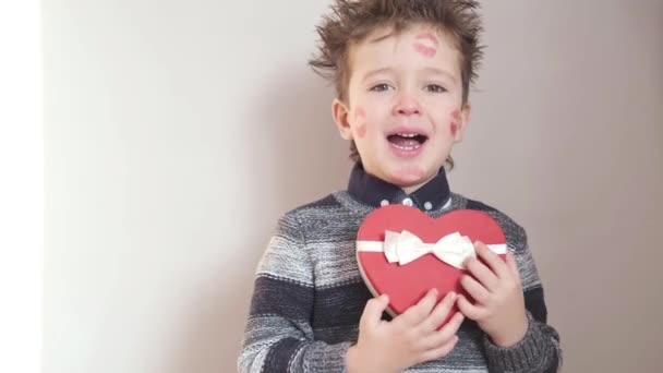 Little boy in sweater with heart gift box and kisses on face valentine day. — Stock Video