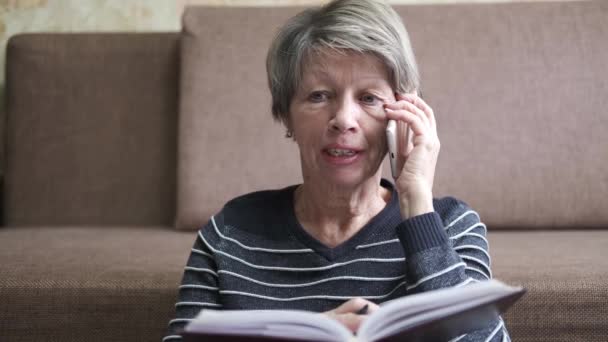 Senior kvinna med telefon och anteckningsbok. Nätarbete. Karantän. — Stockvideo