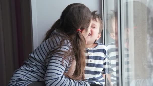 Μικρό χαρούμενο κορίτσι με αγόρι να κάθεται στο παράθυρο. Καραντίνα. Αργή κίνηση. — Αρχείο Βίντεο