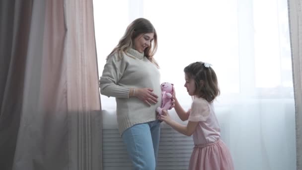 Menina pré-escolar feliz caucasiana com mãe grávida loira. abraços juntos. — Vídeo de Stock