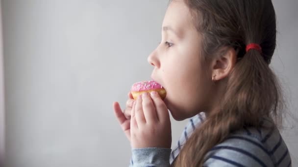 小高加索女孩吃粉红甜甜圈。很高兴见到你靠近点. — 图库视频影像