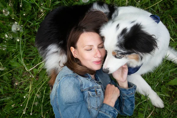 Mladá žena s australským ovčáckým psem ležícím na trávě tváří v tvář — Stock fotografie