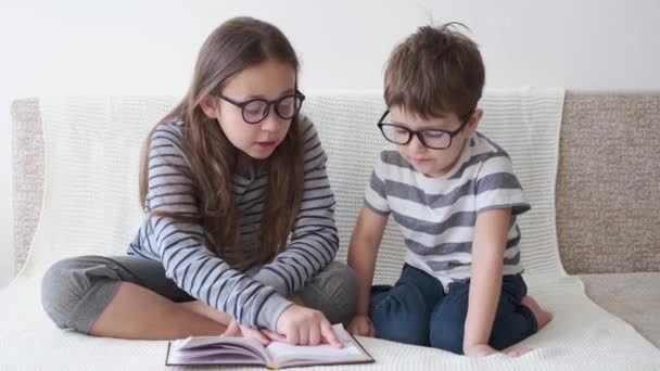 4k. petit mignon caucasien fille et garçon dans lunettes lecture livre — Video