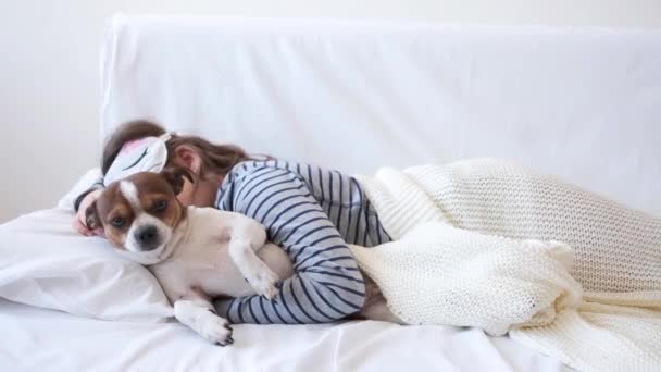 4k. mała dziewczynka i uroczy pies chihuahua w masce oczu śpi w białym łóżku. — Wideo stockowe
