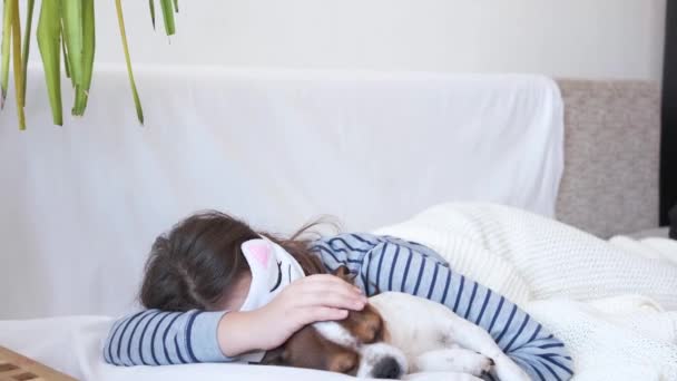 4k. bambina che abbraccia il cane chihuahua in maschera occhi che dorme nel letto bianco. — Video Stock