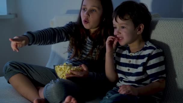 4k. liten kaukasiska flicka och pojke tittar på tv och äter popcorn — Stockvideo