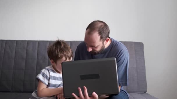 4k. Ο μικρός γιος μαθαίνει διαδικτυακά με τον πατέρα στον καναπέ. Φορητός. — Αρχείο Βίντεο