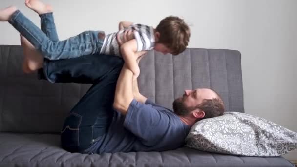 4kだ。興奮した父はソファの上で小さな息子と遊んでいます。幸せな家族 — ストック動画