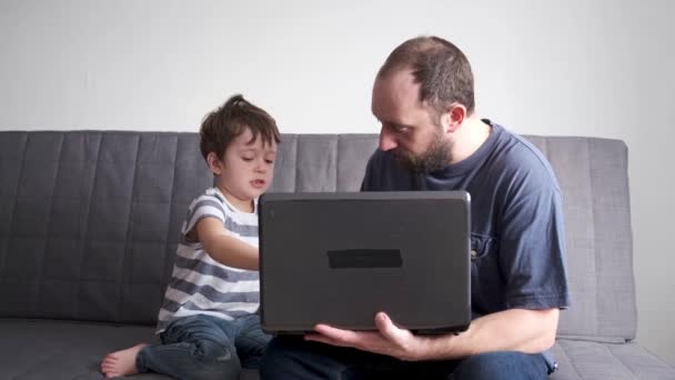 4k. kleiner kaukasischer Sohn lernt online mit Vater auf der Couch. Laptop. — Stockvideo