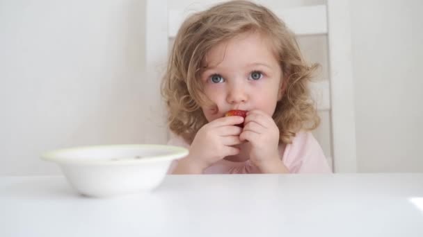 4k. krullend mooi baby meisje eten appel op licht grijs achtergrond — Stockvideo