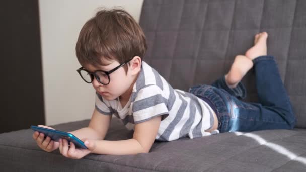 4k. pequeño lindo caucásico chico en gafas estudio en el teléfono — Vídeo de stock