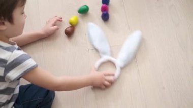 4 bin. Küçük beyaz çocuk renkli yumurtalar ve tavşan kulaklarıyla oynuyor. Paskalya