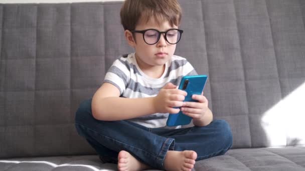 4k. pouco bonito caucasiano pré-escolar menino em óculos estudo no telefone — Vídeo de Stock