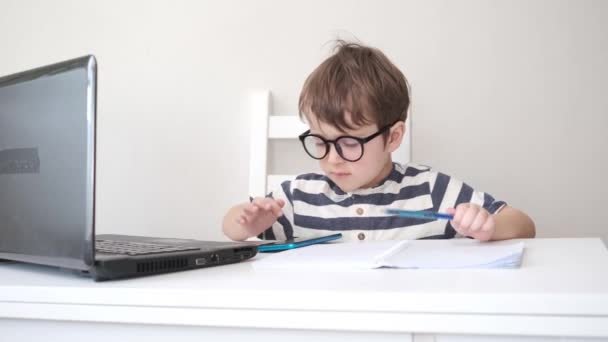 4k. liten söt kaukasiska pojke i glasögon studie i laptop telefon — Stockvideo