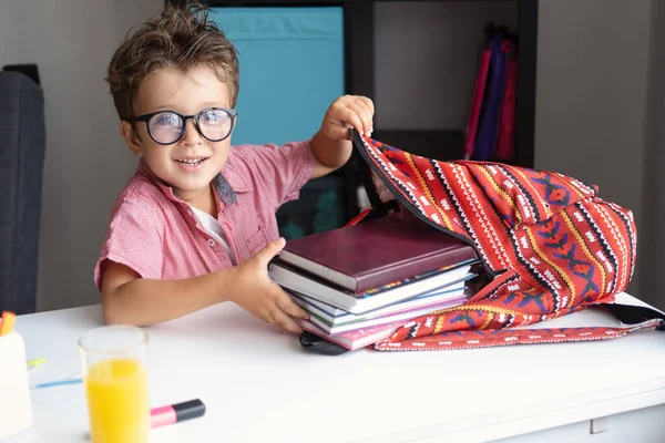 Menino bonito em óculos mochila de embalagem, se preparando para a escola Fotografias De Stock Royalty-Free