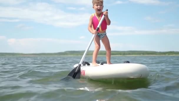 Ufa, Rusia, junio, 13, 2021, preescolar feliz niño aprender a montar en el tablero del charco — Vídeo de stock