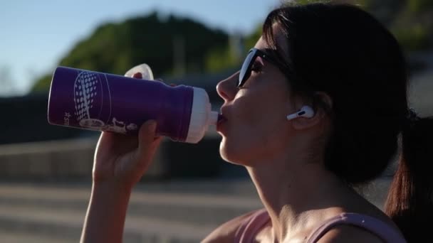 Jovem mulher fitness beber água e ouvir música — Vídeo de Stock