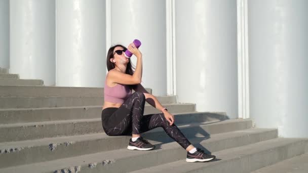 Joven mujer fitness terminar correr, sentarse y beber agua y escuchar música — Vídeo de stock