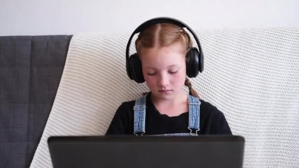Καυκάσια κοκκινομάλλα κοπέλα με ακουστικά χρησιμοποιώντας φορητό υπολογιστή που σπουδάζει στο σπίτι — Αρχείο Βίντεο