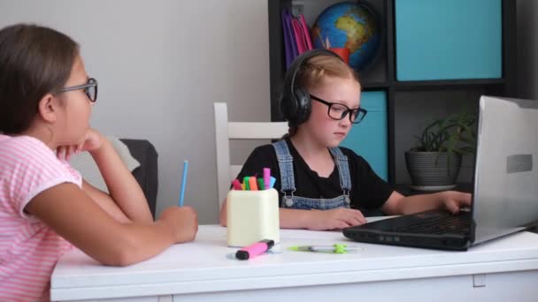 Дві кавказькі дівчата в окулярах використовують ноутбук, який навчається вдома — стокове відео
