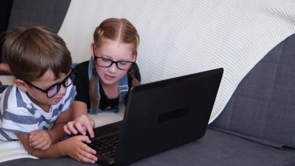 Twee blanke kinderen in bril met laptop die thuis studeert — Stockvideo