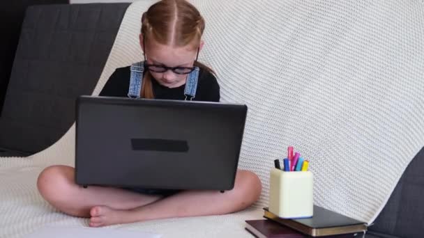 Chica pelirroja caucásica en gafas usando portátil estudiando en casa — Vídeos de Stock