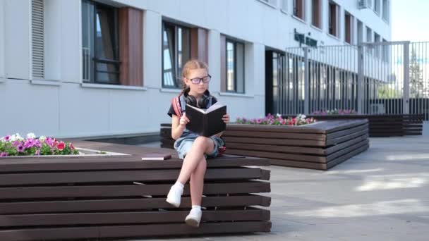 Schattig blank roodharige meisje in bril met rugzak zitten en lees boek — Stockvideo