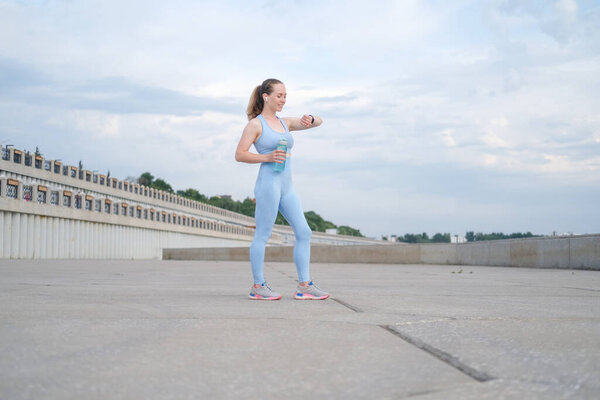 Young fitness woman finish running, checking heart rate in smartwatch