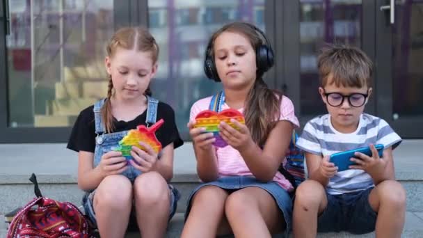 Трое детей с рюкзаком сидят и играют в папат и телефон — стоковое видео