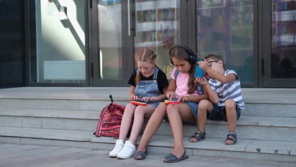 Drie kinderen met rugzak zitten popit en telefoon te spelen — Stockvideo