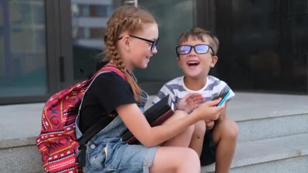 Twee kinderen in brillen met boeken en rugzakpraatjes aan de telefoon — Stockvideo