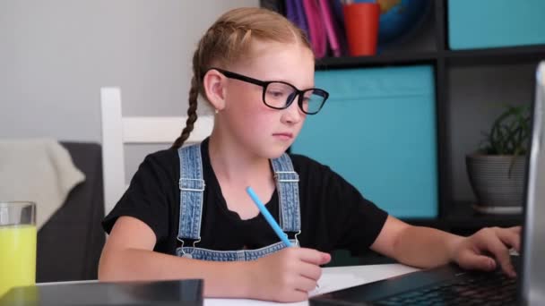 Valkoihoinen punapää tyttö silmälaseissa kannettavan tietokoneen avulla opiskelee kotona — kuvapankkivideo