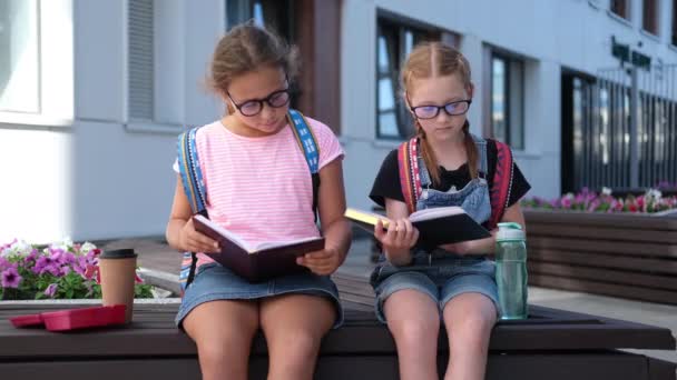 Două fete drăguțe caucaziene în ochelari cu rucsac stau și citesc cartea — Videoclip de stoc