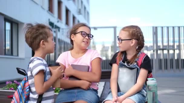 Трое детей с рюкзаком сидят и разговаривают вместе — стоковое видео